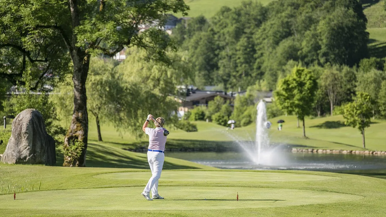 Golfer beim Abschlag am Golfplatz Kitzbühel-Kaps, dahinter ein Teich mit Fontäne