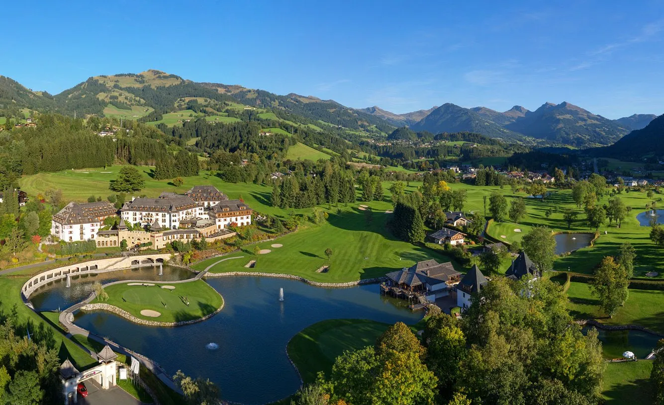 Luftaufnahme des Golfplatzes Kitzbühel mit Teich, Inselgrün und Hotel vor Bergpanorama