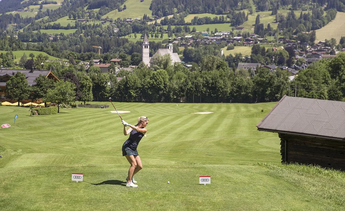 Golferin beim Abschlag am Rasmushof, dahinter Kitzbühel mit der Pfarrkirche