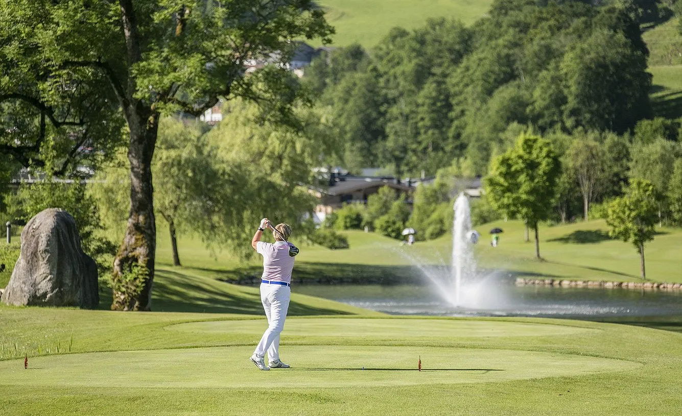 Golfer beim Abschlag vor einem Teich mit Fontäne