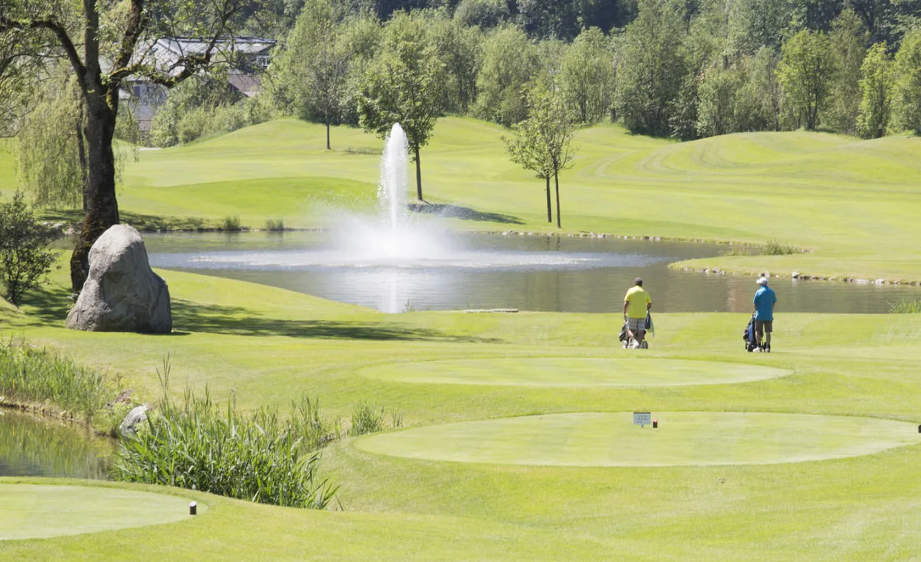 Golfer auf dem Fairway hinter einem Teich mit Fontäne