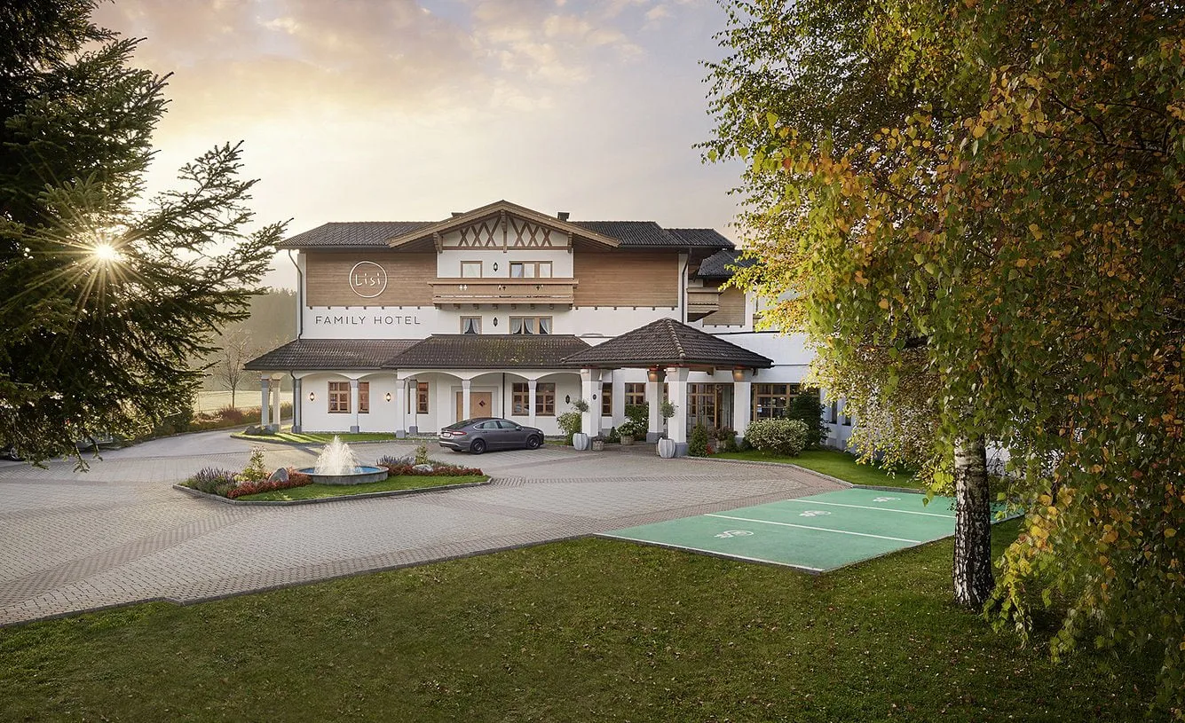 Lisi Family Hotel mit Vorplatz und Brunnen im Abendlicht, davor Wiese und Birke