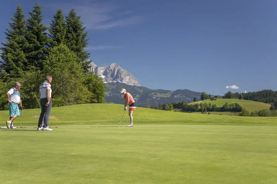 Drei Golfer auf einem Grün, eine Spielerin beim Putten