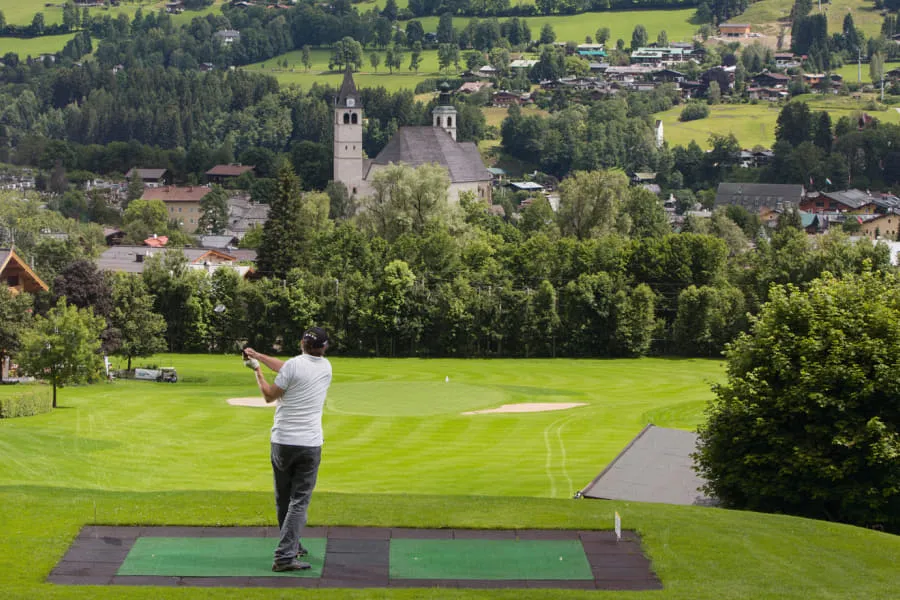 Golfer auf der Abschlagmatte mit Blick auf die Kirchen von Kitzbühel