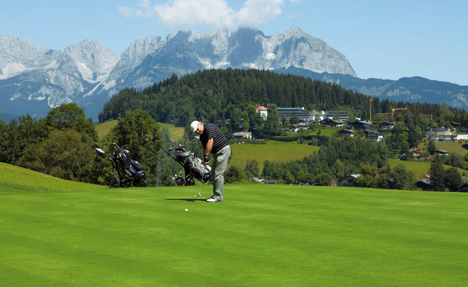 Golfer beim Putten, dahinter Kitzbühel und der Wilde Kaiser