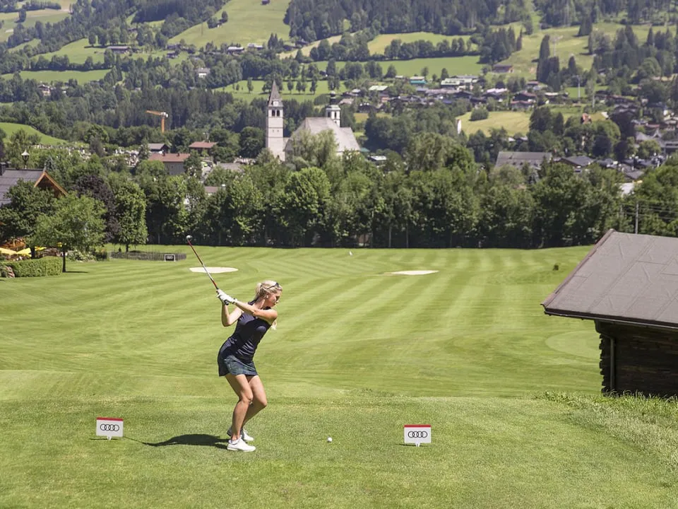 Golferin beim Abschlag am Rasmushof, dahinter Kitzbühel mit der Pfarrkirche