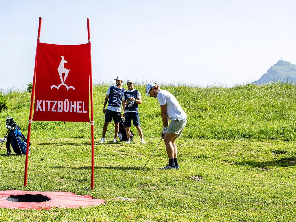 Spieler am Abschlag neben der roten Kitzbühel-Fahne, im Hintergrund das Kitzbüheler Horn